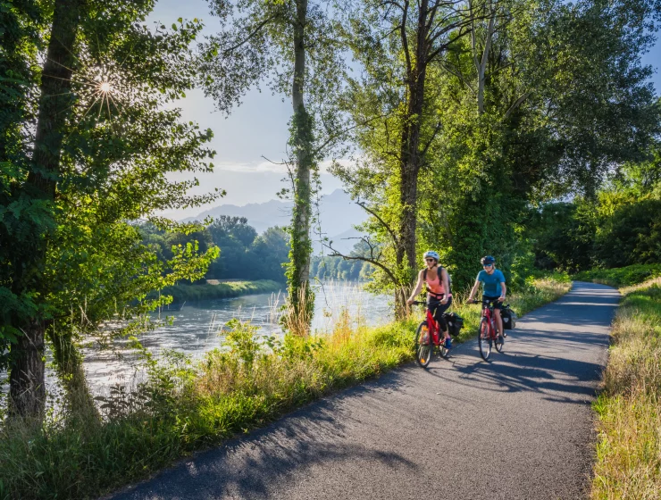 Cyclistes sur la piste cyclable de La Belle Via, traversant des paysages pittoresques entre montagnes, vignobles et rivières, offrant une escapade vélo immersive en Isère.