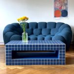 Table basse artisanal carrelée en bleu, devant un canapé aux formes arrondies dans un salon moderne