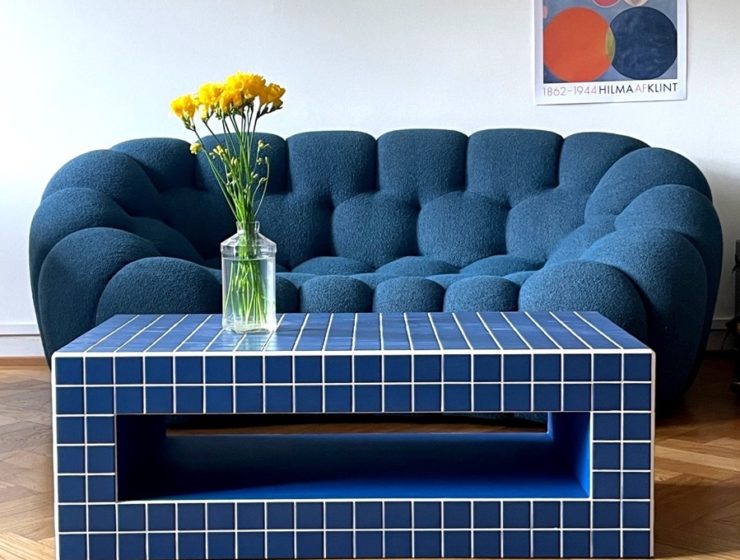 Table basse artisanal carrelée en bleu, devant un canapé aux formes arrondies dans un salon moderne