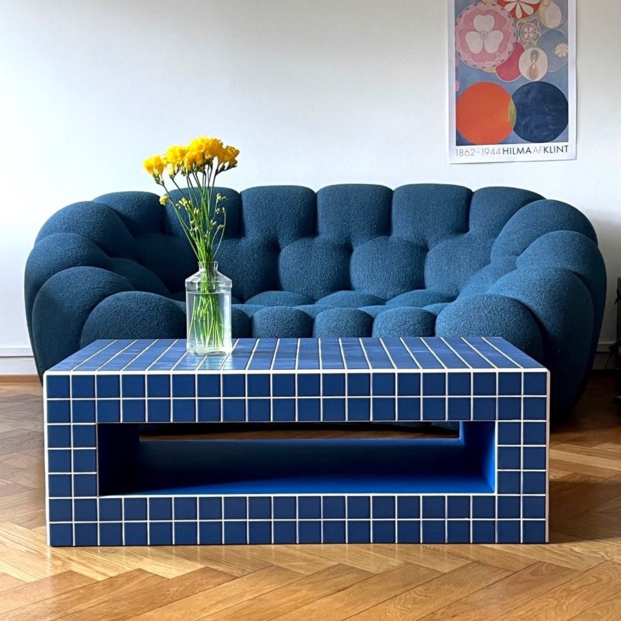 Table basse artisanal carrelée en bleu, devant un canapé aux formes arrondies dans un salon moderne