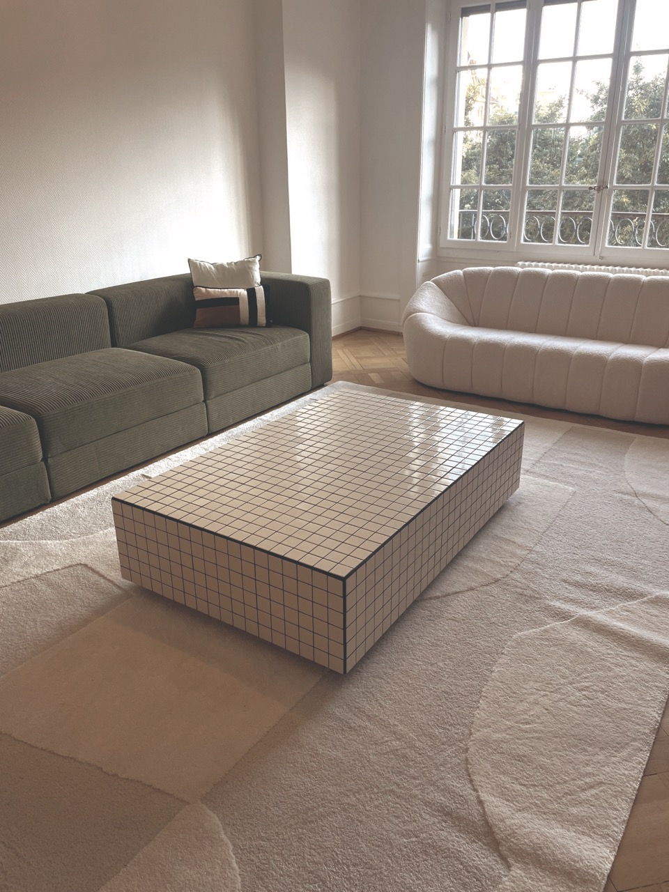 Table basse rectangulaire carrelée en crème dans un salon lumineux avec canapé vert et canapé beige