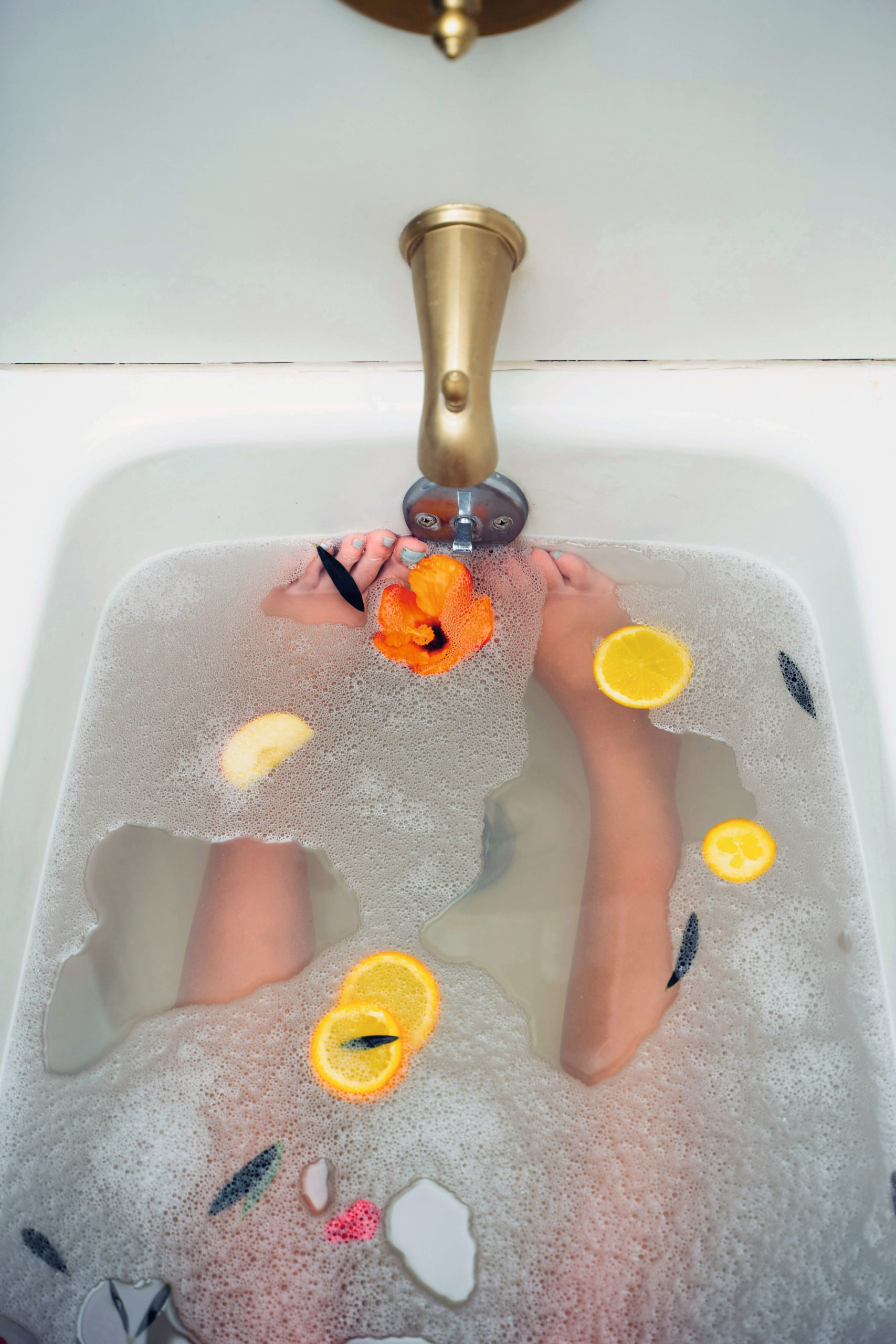 Vue plongeante sur un bain moussant avec agrumes, fleurs et pétales autour des jambes