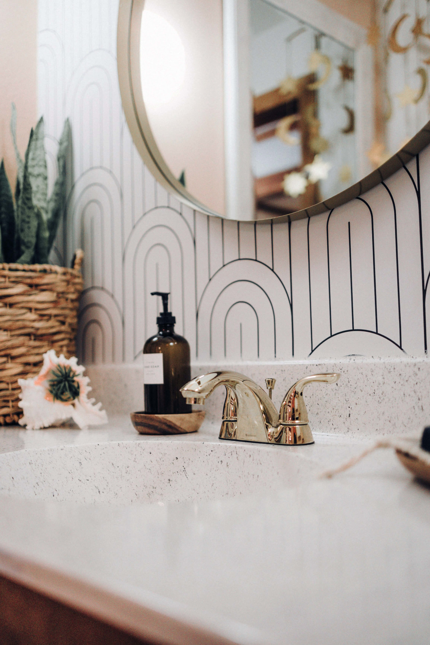 Lavabo clair avec robinetterie dorée, miroir rond et plante dans une salle de bains lumineuse